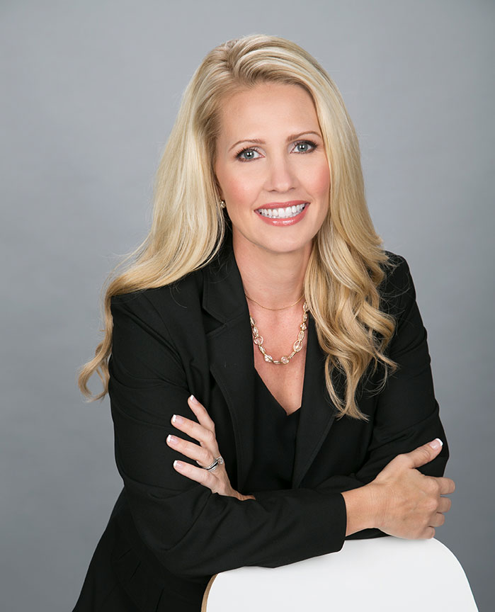 corporate headshot of blond real estate agent woman wearing balc suit smiling with folded arms